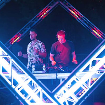Two Dj's playing techno music on the futuristic stage at summer night concert.